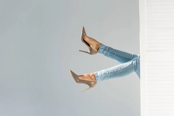 Vista ritagliata della donna in jeans e scarpe con tacco alto marroni su sfondo grigio — Foto stock