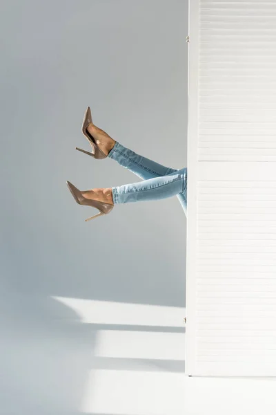 Partial view of woman in jeans and high-heeled shoes on grey background — Stock Photo