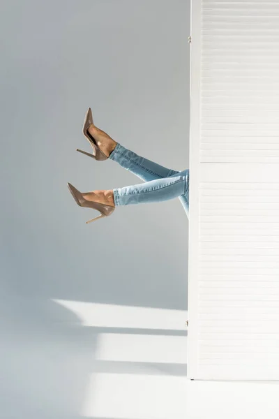 Vista parziale della donna in jeans e scarpe con tacco alto su sfondo grigio — Foto stock