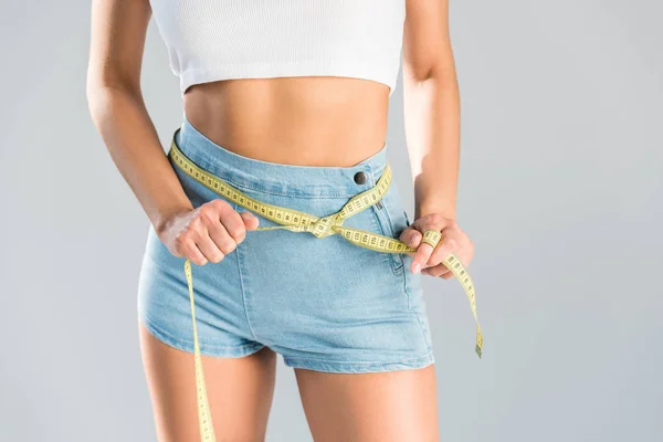 Cropped view of woman holding measuring tape on waist isolated on grey — Stock Photo