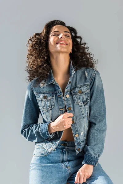 Mujer alegre en chaqueta de mezclilla riendo con los ojos cerrados sobre fondo gris - foto de stock