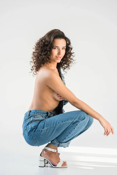 Chica topless rizado en jeans sentado sobre fondo gris - foto de stock