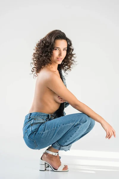 Fille seins nus bouclés en jeans assis sur fond gris — Photo de stock