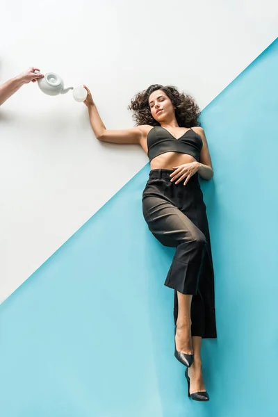 Cropped view of hand with teapot and curly woman with cup on white & blue background — Stock Photo