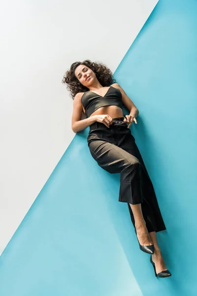 Jovem mulher elegante em roupas pretas deitado na superfície branca e azul — Fotografia de Stock