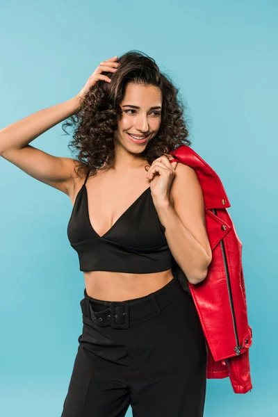 Joyful brunette girl holding red jacket on blue background — Stock Photo