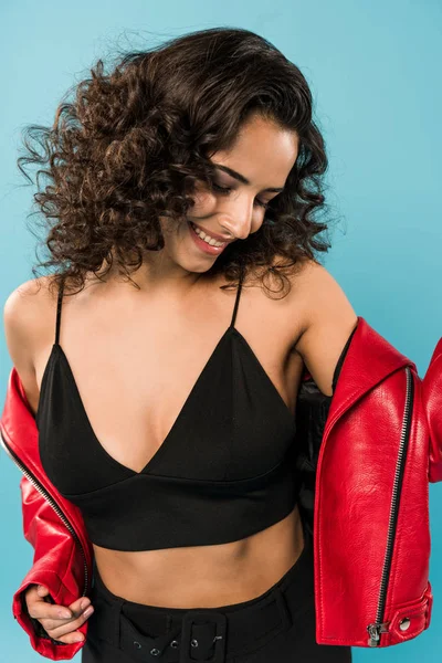 Sonriente chica rizada quitándose la chaqueta roja sobre fondo azul - foto de stock