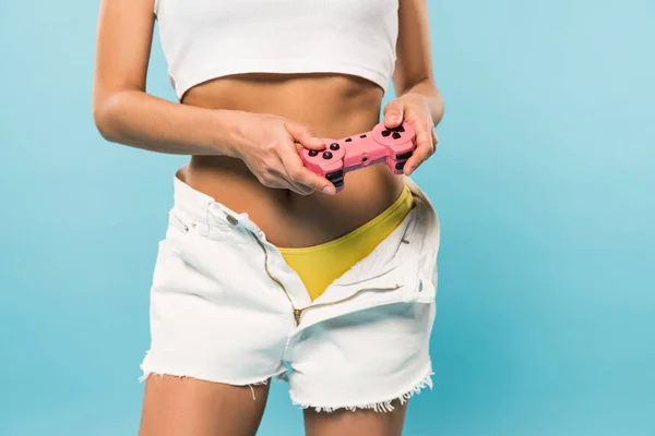 Vista ritagliata di ragazza sexy in pantaloncini che tengono il controller su sfondo blu — Foto stock
