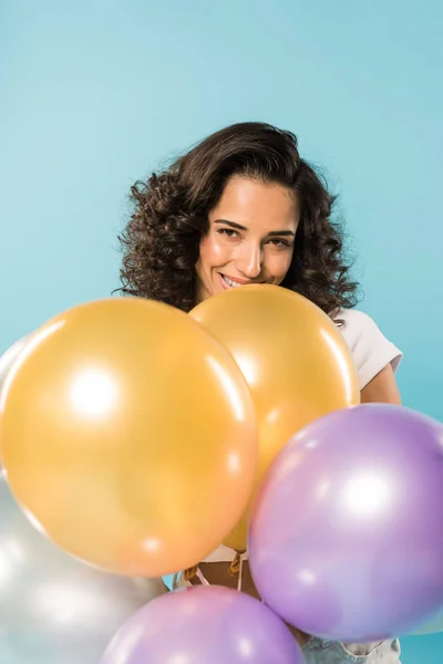 Bonita chica morena sosteniendo globos de aire y sonriendo sobre fondo azul - foto de stock