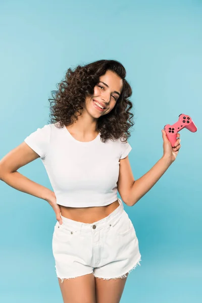 Schlanke, lachende Frau in kurzen Hosen mit Gamepad auf blauem Hintergrund — Stockfoto