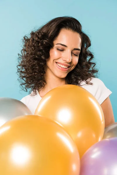 Fröhliche lockige Mädchen mit geschlossenen Augen lächeln und halten Luftballons auf blauem Hintergrund — Stockfoto