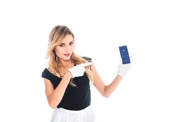 Femme de ménage en uniforme noir et gants pointant du doigt sur smartphone isolé sur blanc — Photo de stock