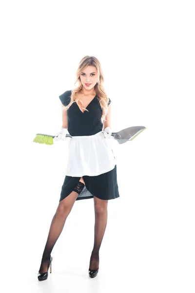 Jolie femme de ménage en uniforme noir, tablier, bas debout avec balai et cuillère sur fond blanc — Photo de stock
