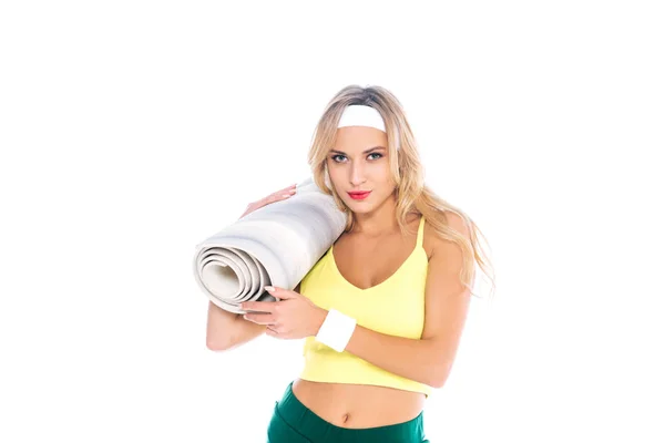 Entraîneur de fitness blonde en short vert et singulet jaune tenant tapis de yoga isolé sur blanc — Photo de stock
