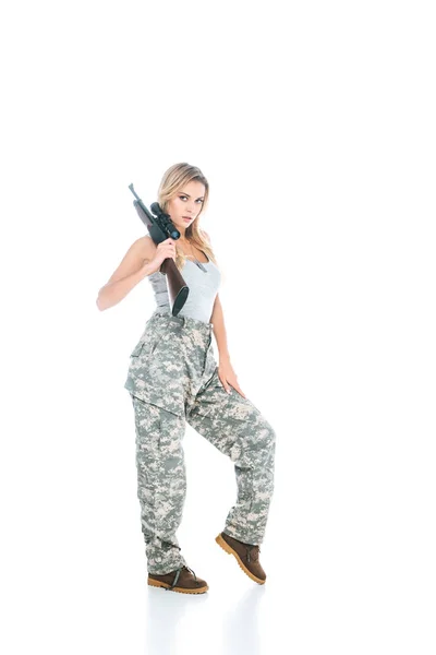 Blonde militarywoman in grey t-shirt and camouflage pants standing with rifle on white background — Stock Photo