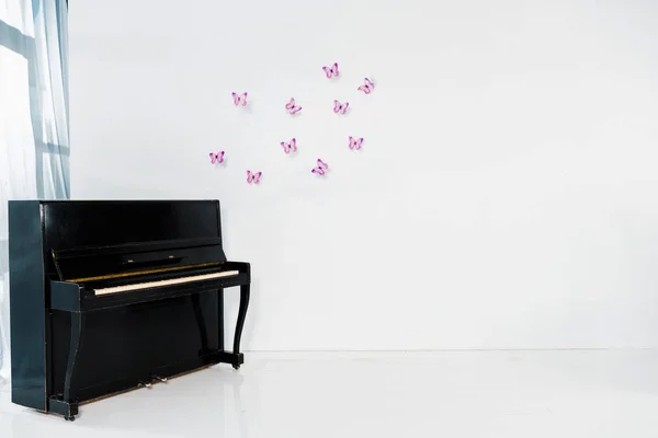 Pianoforte nero su sfondo bianco con farfalle viola e spazio copia — Foto stock