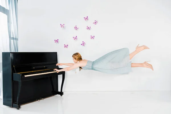 Floating girl in blue dress playing black piano on white background — Stock Photo