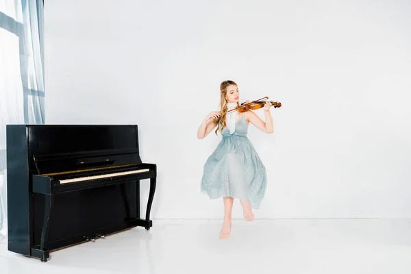 Fille flottante en robe bleue jouant du violon sur fond blanc — Photo de stock