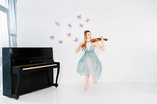 Floating girl in blue dress playing violin on white background with purple butterflies and copy space — Stock Photo