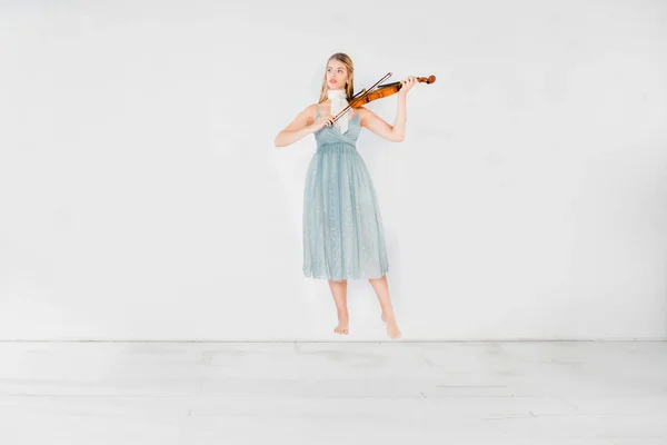 Menina flutuante em vestido azul tocando violino no fundo branco com espaço de cópia — Fotografia de Stock