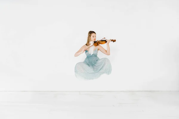 Floating girl in blue dress playing violin on white background — Stock Photo