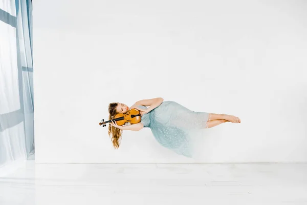 Menina em vestido azul dormindo no violino no ar no fundo branco — Fotografia de Stock