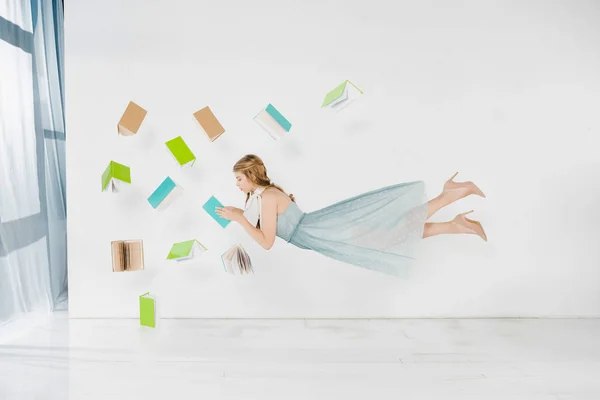 Menina flutuante no livro de leitura vestido azul no ar no fundo branco — Fotografia de Stock