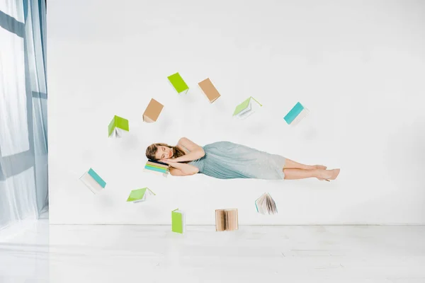 Chica flotante en vestido azul durmiendo en el libro en el aire sobre fondo blanco - foto de stock