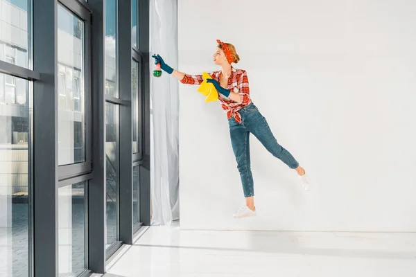 Menina flutuante em jeans e xadrez janelas de limpeza camisa com pano e spray — Fotografia de Stock