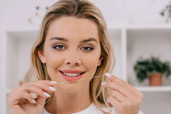 Bela mulher sorridente segurando fio dental e olhando para a câmera — Fotografia de Stock