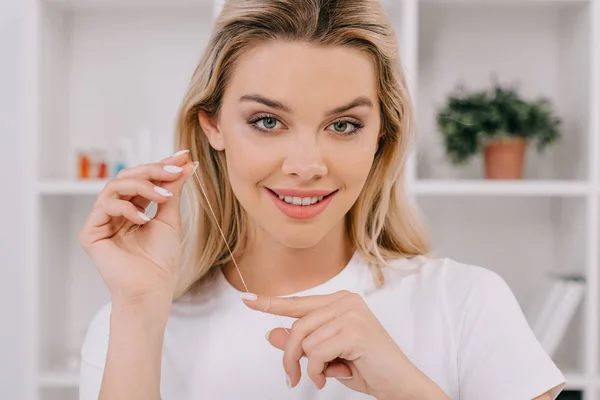 Bela mulher sorridente segurando fio dental e olhando para a câmera — Fotografia de Stock