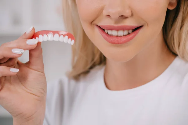 Recortado vista de sonriente mujer sosteniendo dientes cubierta — Stock Photo