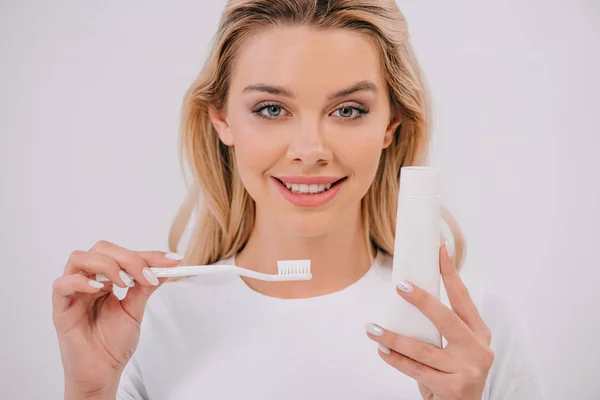 Hermosa mujer mirando a la cámara mientras sostiene el cepillo de dientes y pasta de dientes con espacio de copia aislado en blanco - foto de stock