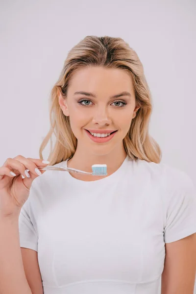 Hermosa mujer sonriente sosteniendo el cepillo de dientes y mirando a la cámara aislada en blanco - foto de stock