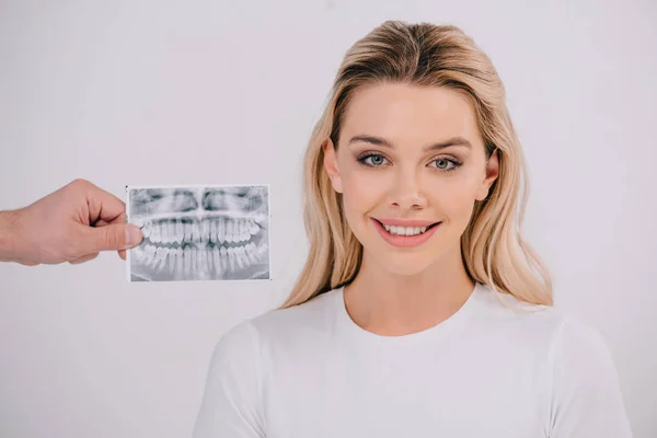 Male hand holding teeth x-ray while beautiful smiling woman in t-shirt looking at camera isolated on white — Stock Photo