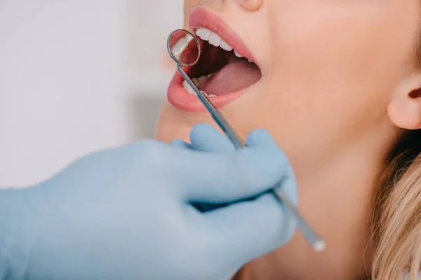 Vista parcial del dentista examinando los dientes de la mujer joven con espejo de la boca - foto de stock