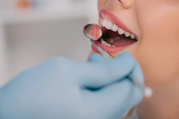 Vue recadrée du dentiste examinant les dents de la jeune femme avec miroir buccal — Photo de stock