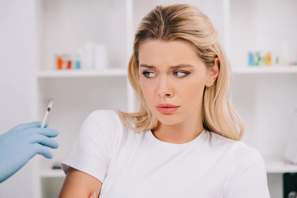 Налякана жінка дивиться на стоматолога, який тримає шприц з місцевою анестезією — стокове фото