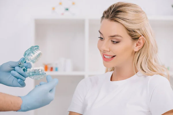 Beautiful smiling woman looking at orthodontist holding jaw model during consultation in clinic — Stock Photo