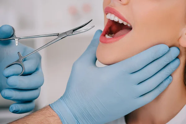 Vista ritagliata del dentista in guanti di lattice con strumento dentale esaminare i denti della donna in clinica — Foto stock