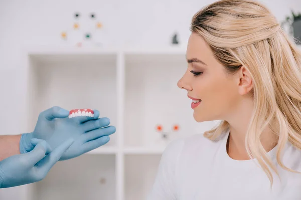 Beautiful woman looking at dentist in latex gloves holding teeth cover in clinic — Stock Photo