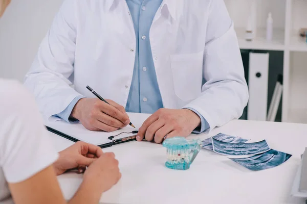 Обрізаний вид ортодонта, що пише діагноз під час консультації з жінкою в клініці — стокове фото