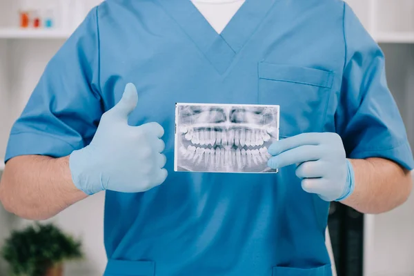 Ausgeschnittene Ansicht eines Kieferorthopäden, der Daumen nach oben zeigt und Zähne röntgt in Klinik — Stockfoto