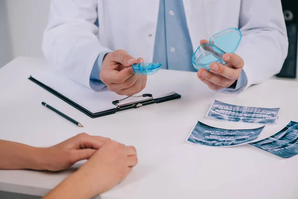 Vista recortada del ortodoncista que presenta los aparatos dentales de entrenamiento durante la consulta con la mujer - foto de stock