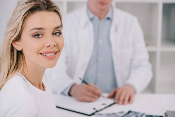 Foco seletivo da mulher bonita olhando para a câmera durante a consulta com o dentista masculino na clínica — Fotografia de Stock