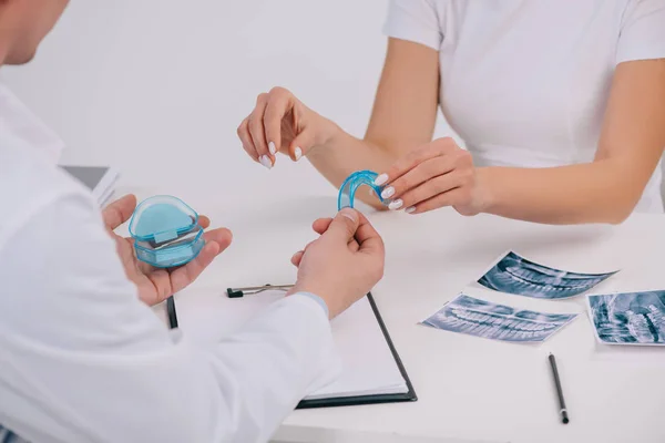 Vista recortada de la mujer que toma aparatos dentales entrenador de ortodoncista durante la cita aislado en blanco - foto de stock