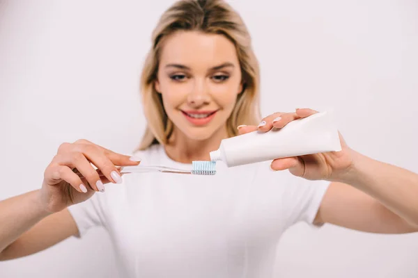 Hermosa mujer sonriente poniendo pasta de dientes en cepillo de dientes aislado en blanco - foto de stock