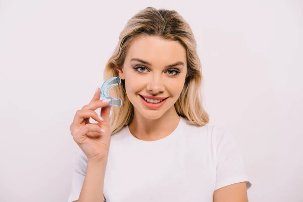 Красива усміхнена жінка в білій футболці тримає ортодонтичні тренувальні зубні брекети ізольовані на білому — Stock Photo