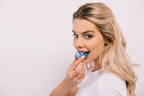 Schöne Frau, die in die Kamera schaut, während sie Kieferorthopädietrainer Zahnspangen anzieht, isoliert auf weiß mit Kopierraum — Stockfoto