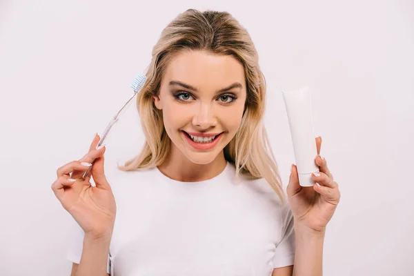 Hermosa mujer sonriente sosteniendo cepillo de dientes y pasta de dientes con espacio de copia aislado en blanco - foto de stock